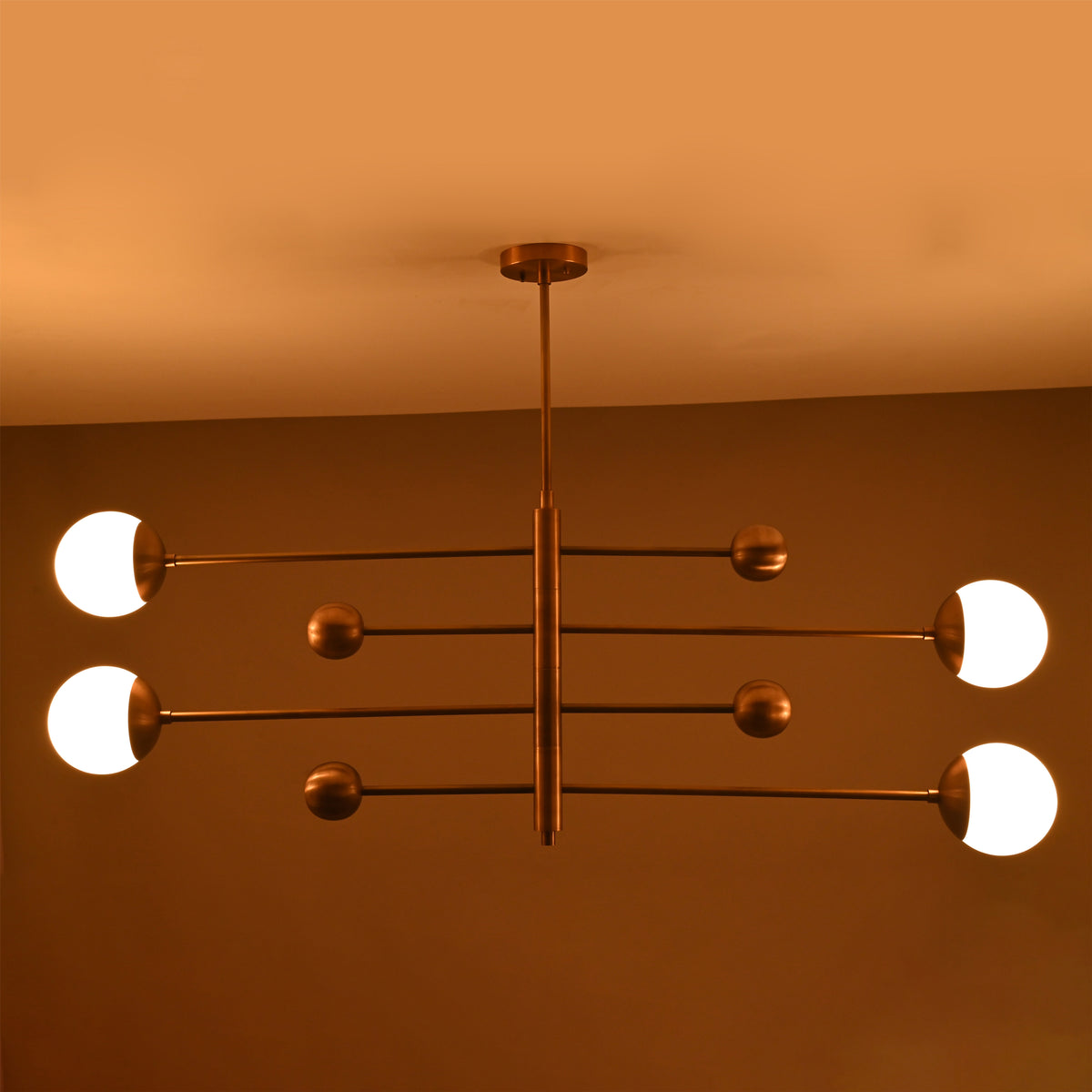 Modern linear brass chandelier glowing in warm ambient light with four glass globe diffusers.