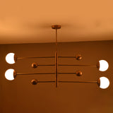 Modern linear brass chandelier glowing in warm ambient light with four glass globe diffusers.