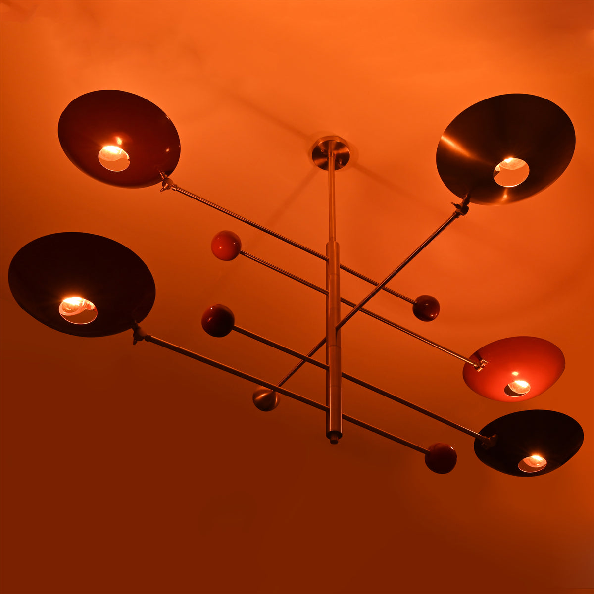 Warm glowing lighting effect of modern brass mobile chandelier with red bowl shades, highlighting ambient indirect illumination.