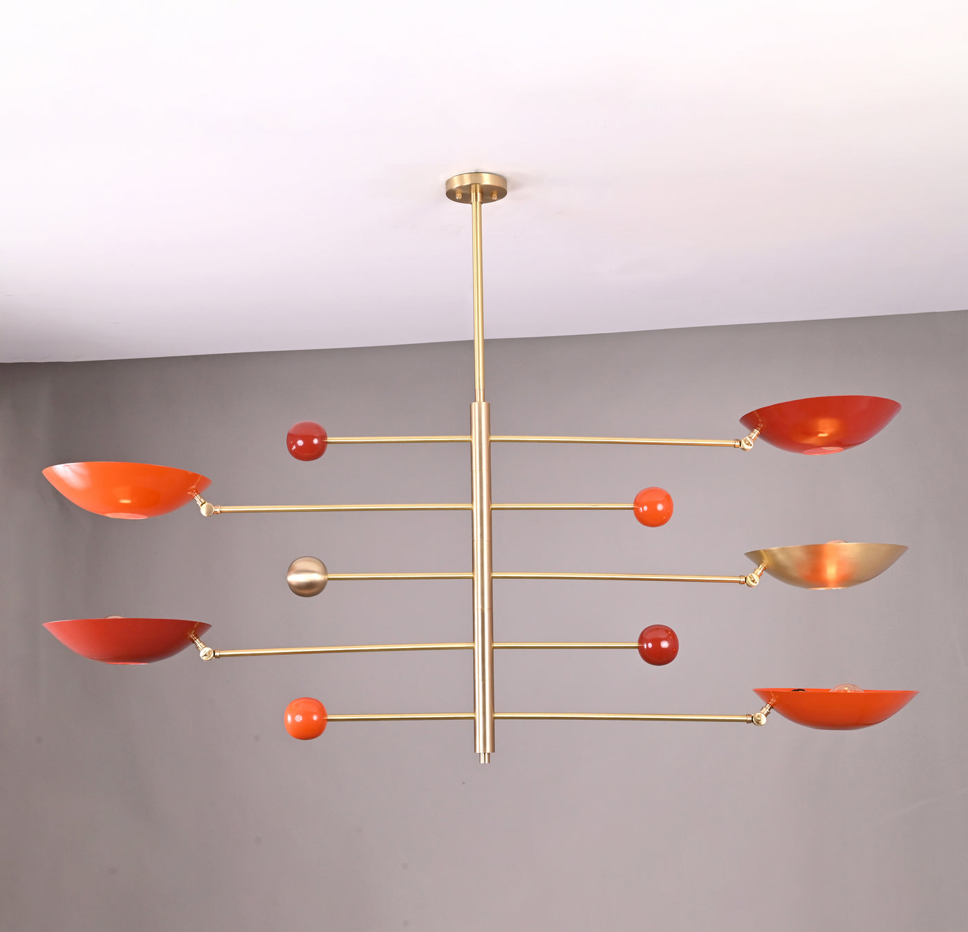 Modern brass mobile chandelier with red bowl-shaped shades featuring sculptural balanced arms handcrafted by Brass Leaf Studio.