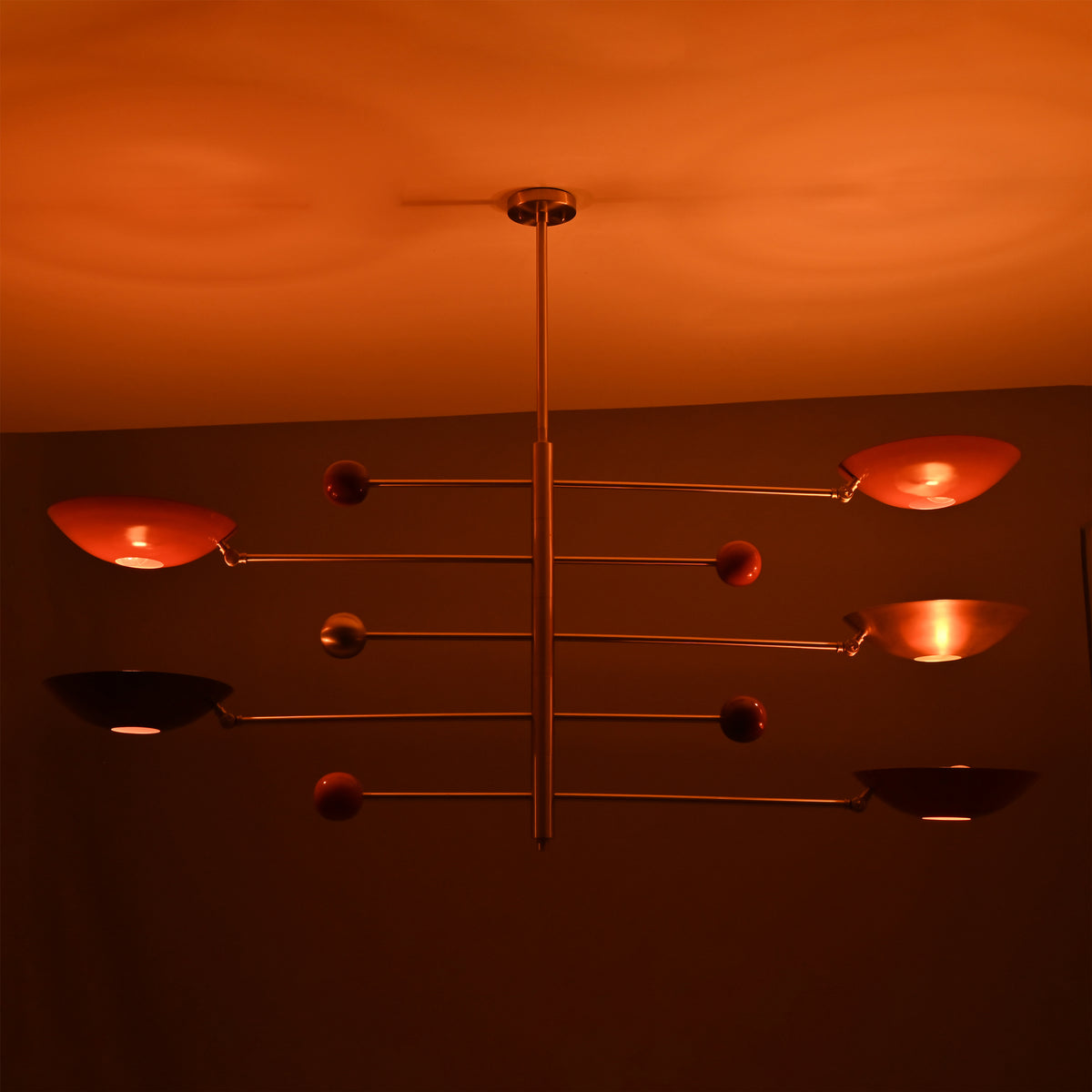 Sculptural modern brass mobile lighting fixture with red bowl shades casting warm ambient illumination.