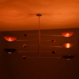 Sculptural modern brass mobile lighting fixture with red bowl shades casting warm ambient illumination.