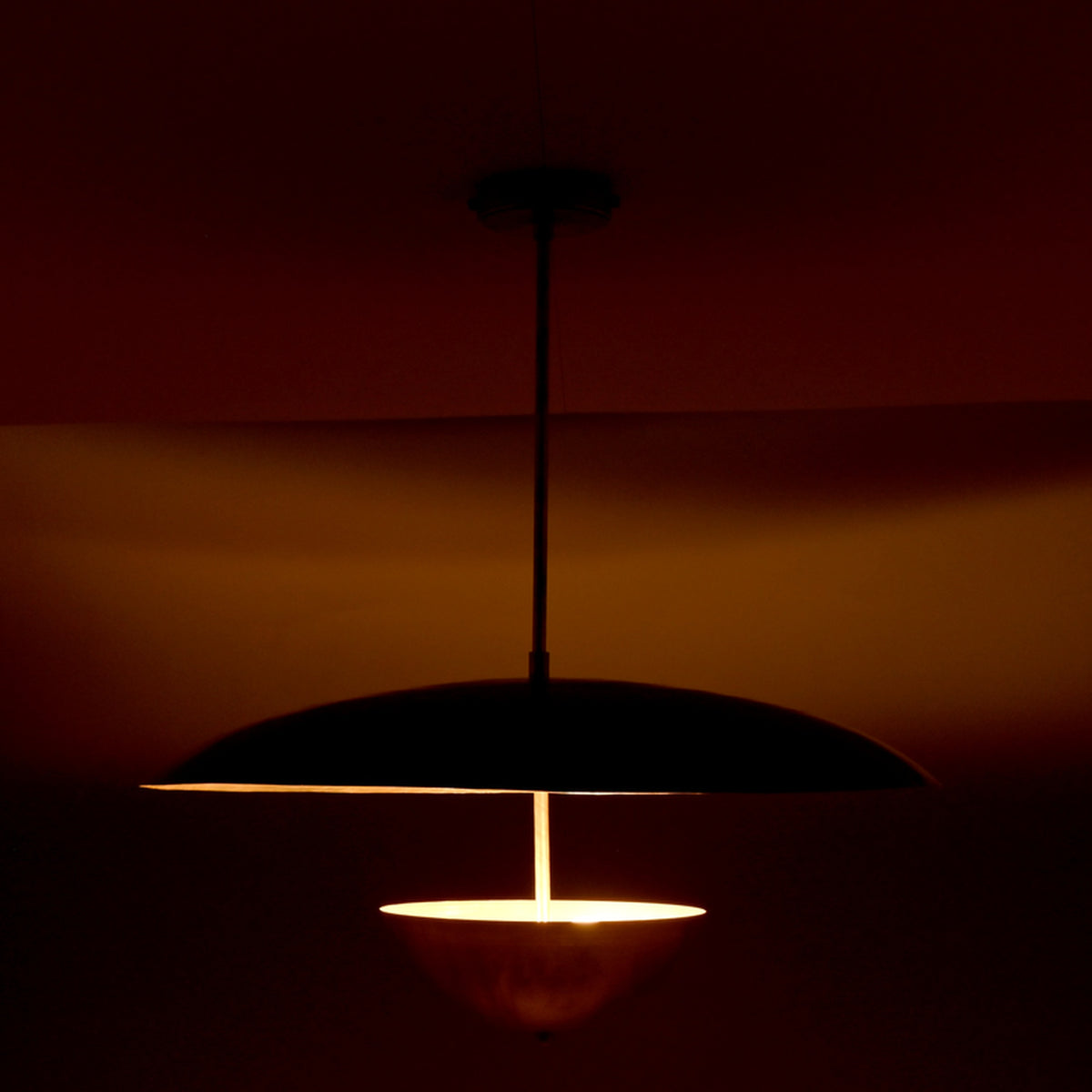 Evening profile view of modern brass pendant with dual shades producing soft, diffused ambient lighting.