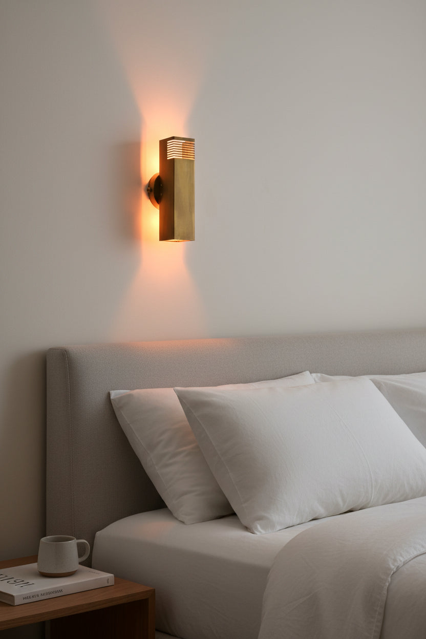 Modern brass tube wall sconce shown illuminated with decorative slotted detail and warm light pattern on the wall