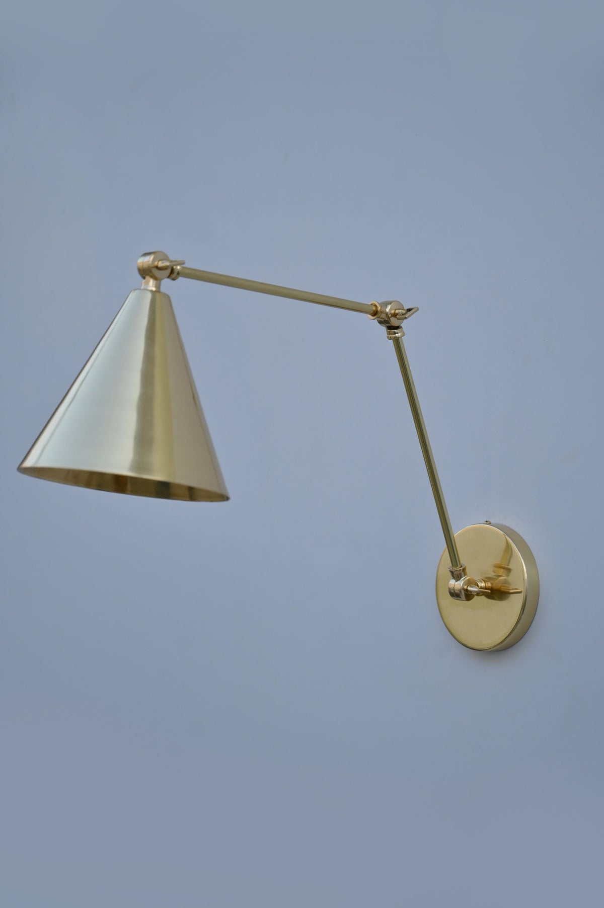 Modern brass wall light with cone shade and adjustable arm for directional lighting