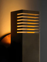 Angled close-up of modern brass wall sconce highlighting illuminated slotted layers and warm lighting effect