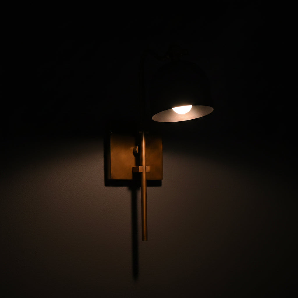 Modern classic brass wall light with warm downward glow, curved arm design, and slim vertical wall-mounted profile