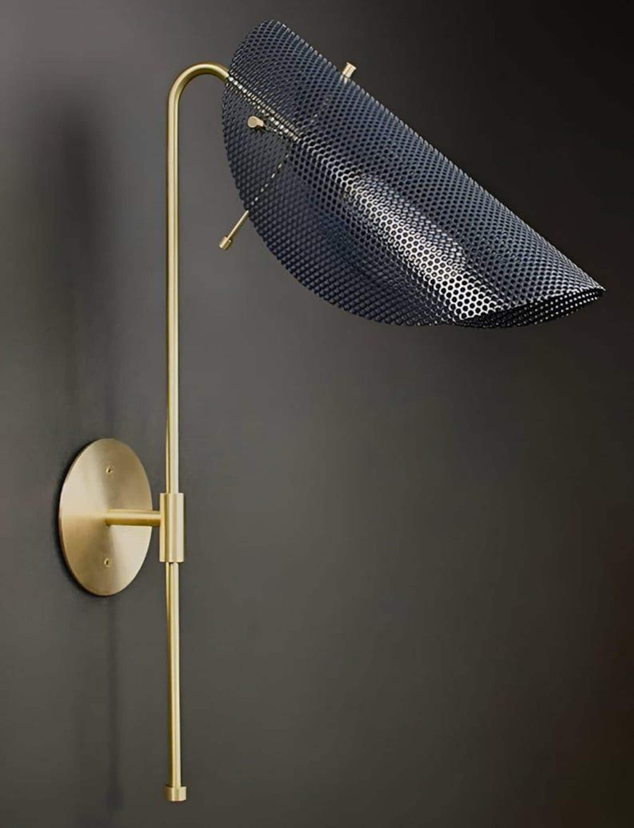 Curved brass wall lamp with perforated metal shade casting warm ambient light in a modern interior