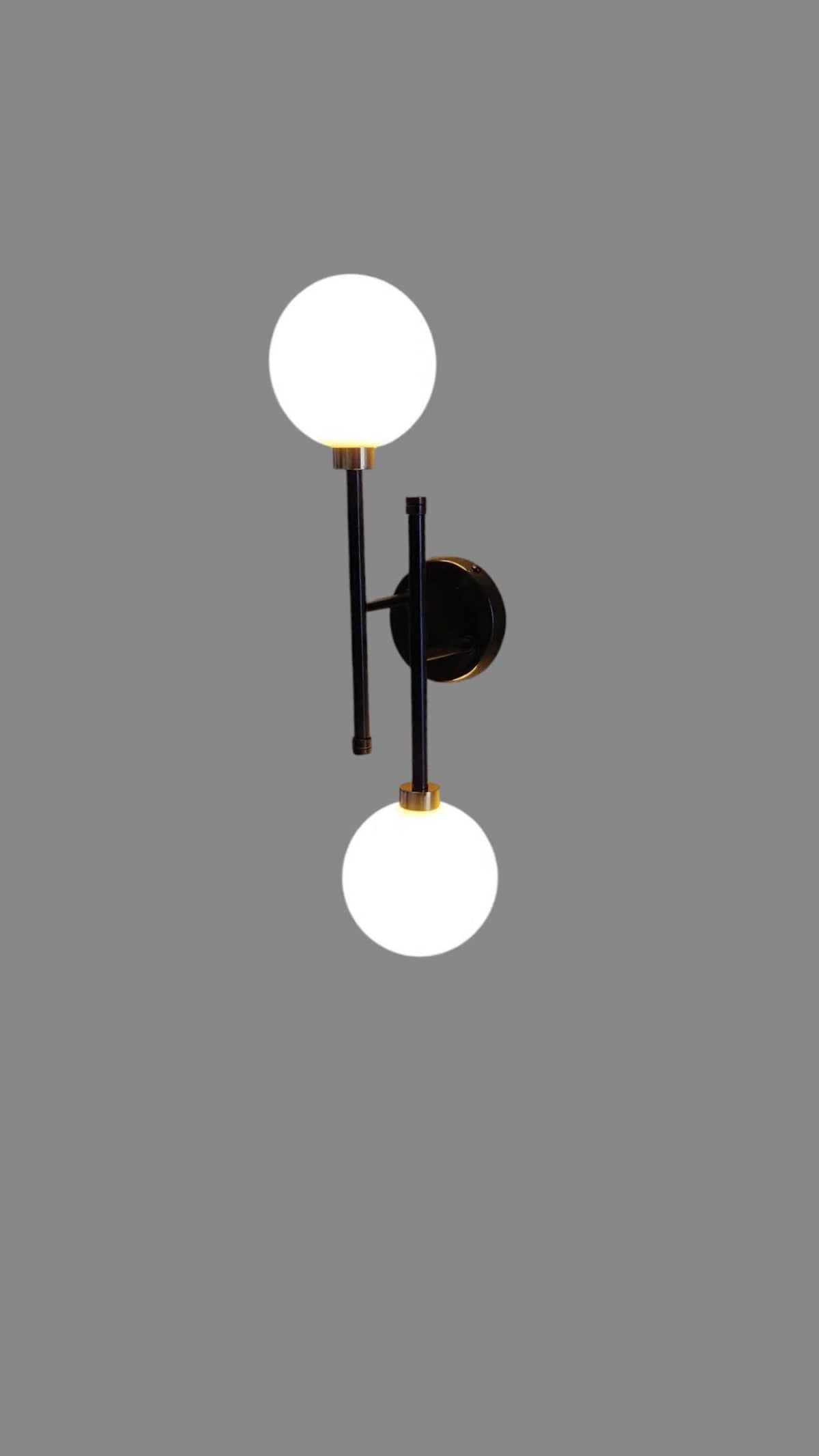 Modern black and brass double globe wall sconce with opal glass shades, vertical alignment design for elegant interior lighting.