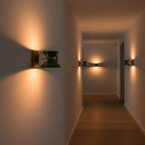 Modern green wall sconce with brass movable arm creating warm focused light on the wall