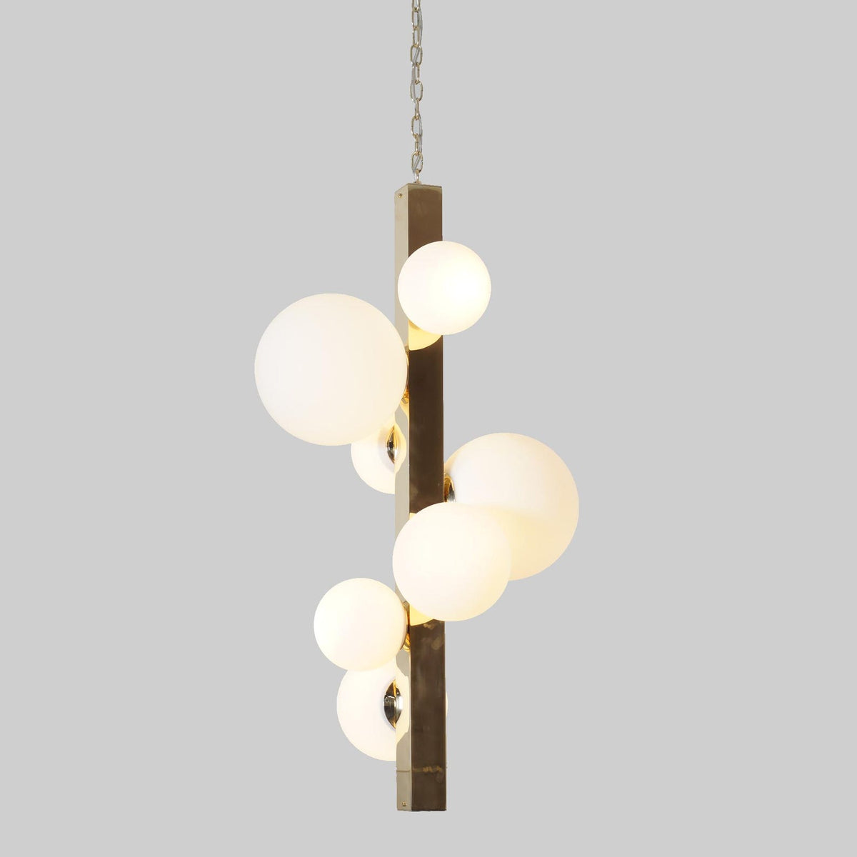 Contemporary pendant light with solid brass column and multiple glowing frosted globes.