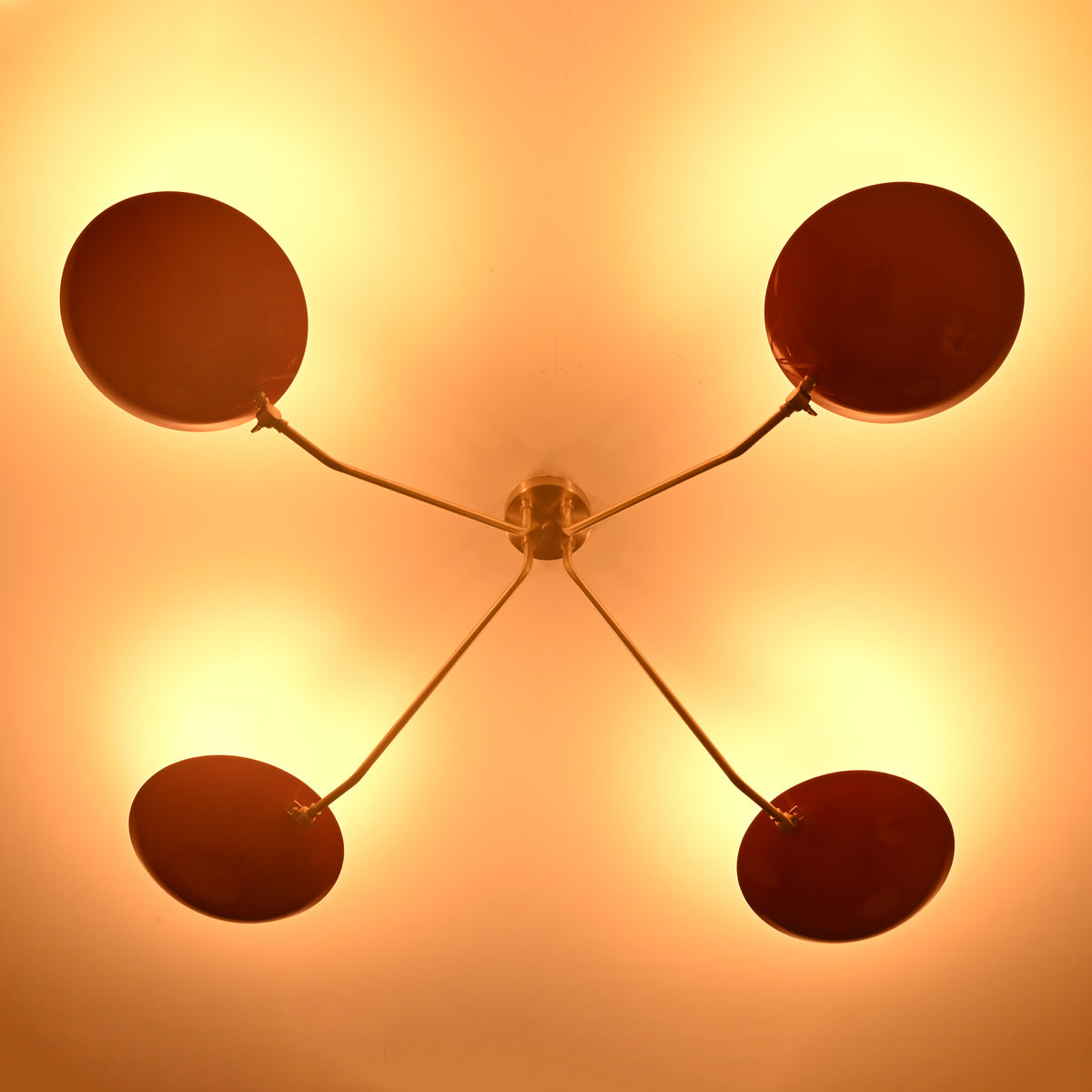 Modern red disc brass ceiling light photographed in low light environment highlighting warm glow and sculptural design.