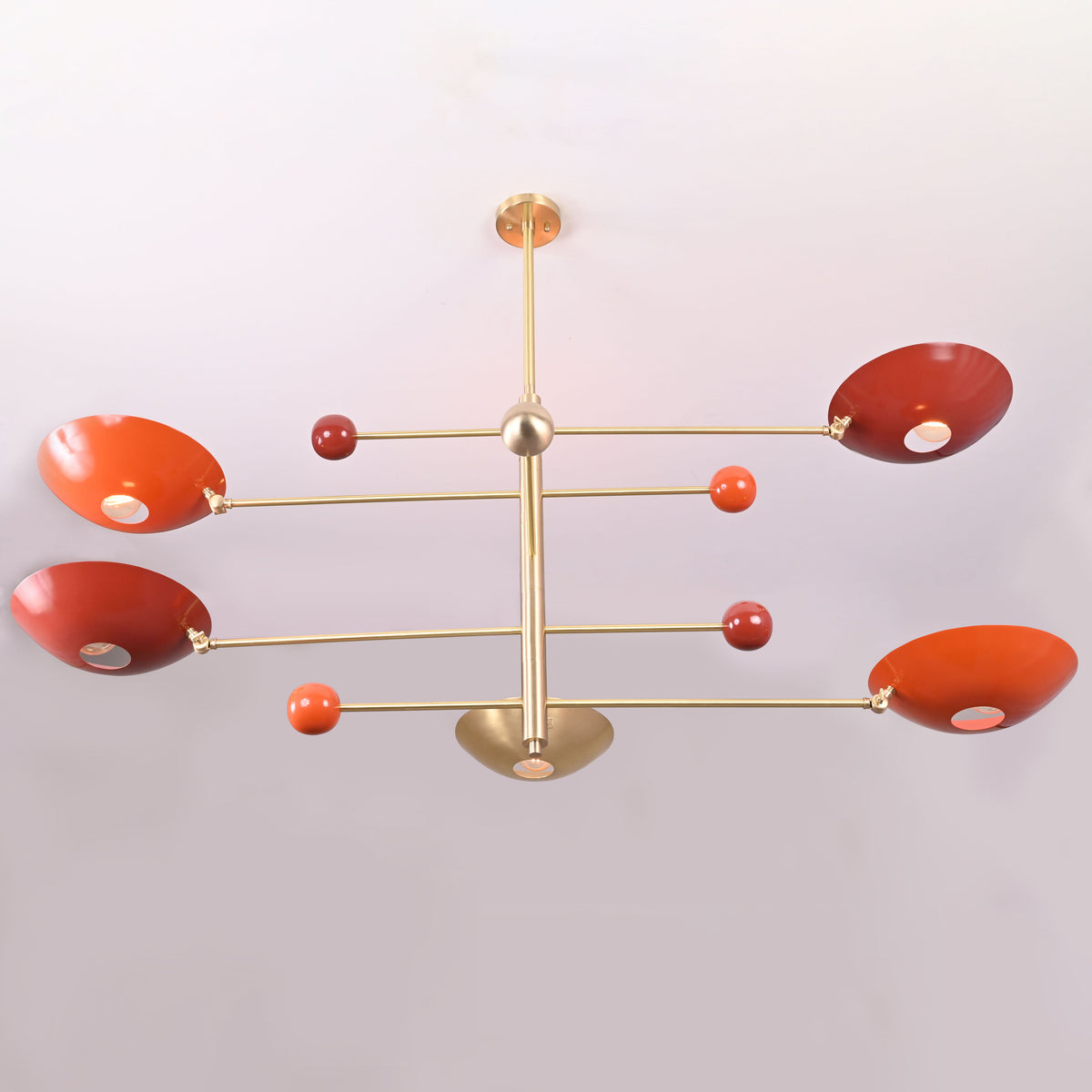 Modern sculptural chandelier in brushed brass with red bowl shades providing upward indirect lighting.