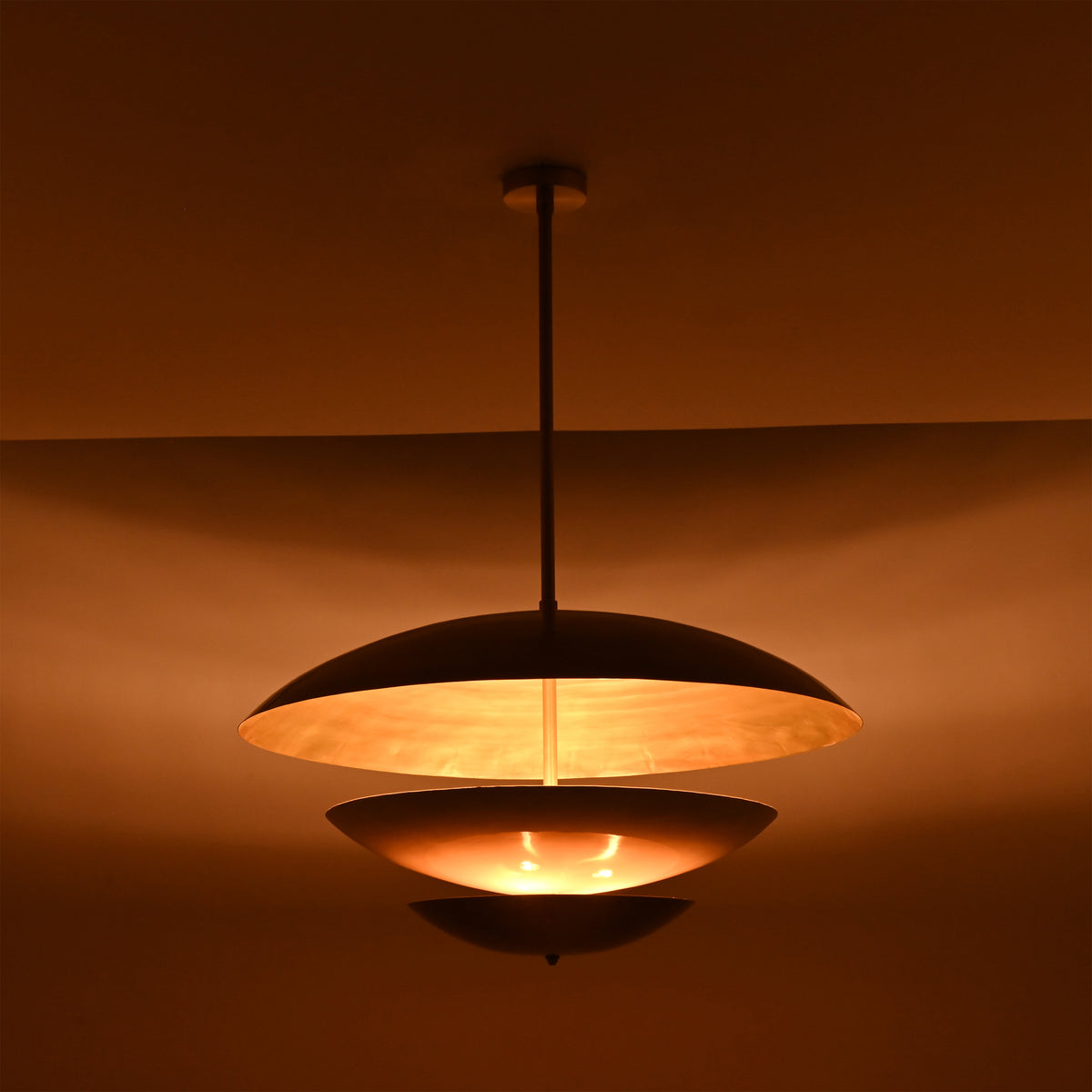 Modern tiered pendant light closeup showing sculptural layered discs and warm illuminated diffuser detail
