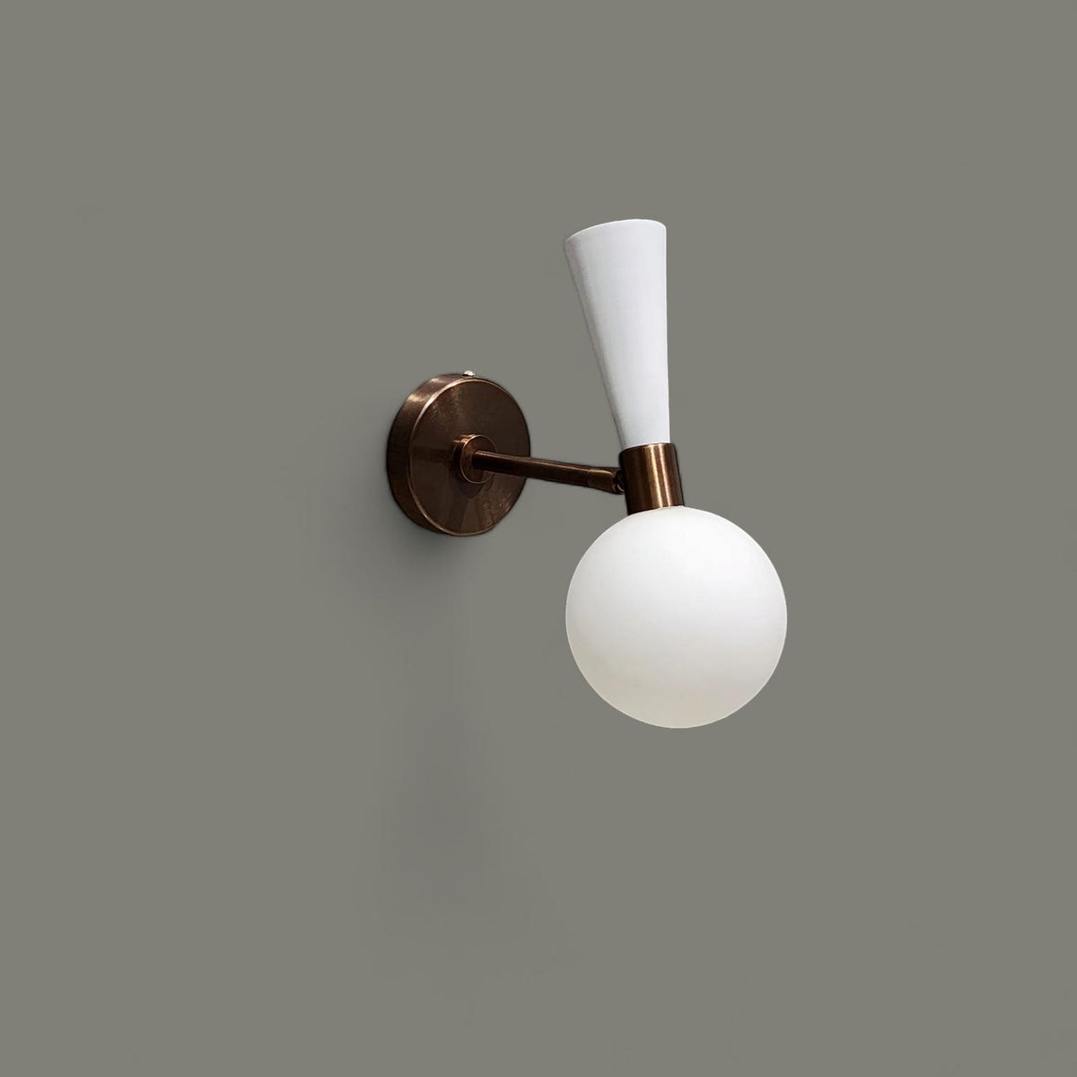 Side view of modern two-tone brass and white wall sconce with frosted glass globe shade