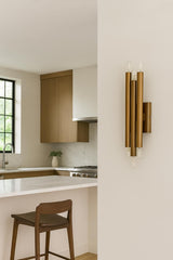 Modern vertical brass wall sconce with six exposed bulbs installed in contemporary kitchen interior creating architectural statement lighting