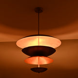 Closeup view of the lit multi-layer brass chandelier showing warm ambient glow from its copper-finish bowl elements.