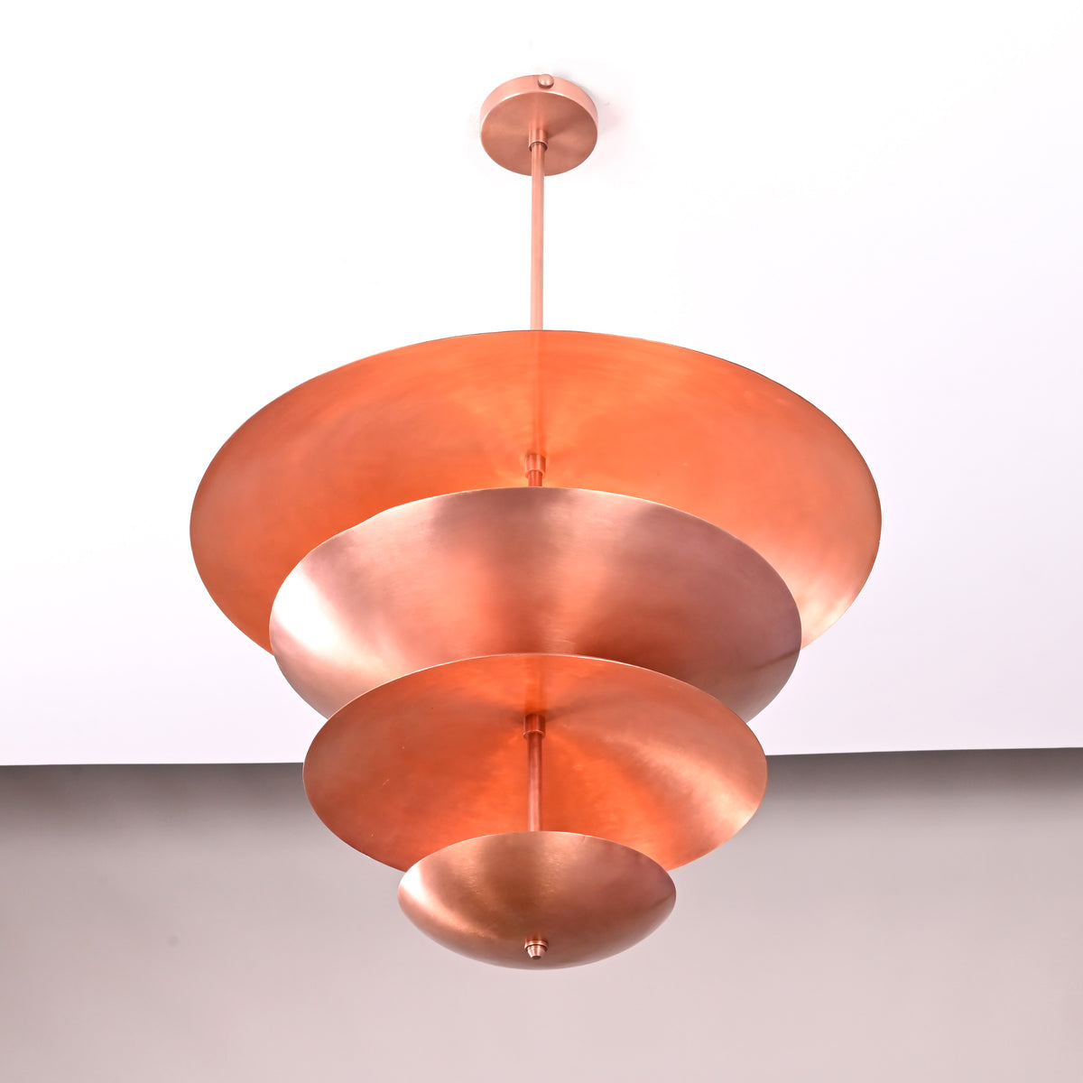 Bottom view of the brass multi-tier chandelier showing concentric circular shades in a polished copper finish.