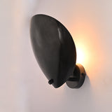 Noir Petal solid brass wall sconce shown in living room with warm halo glow behind curved shield