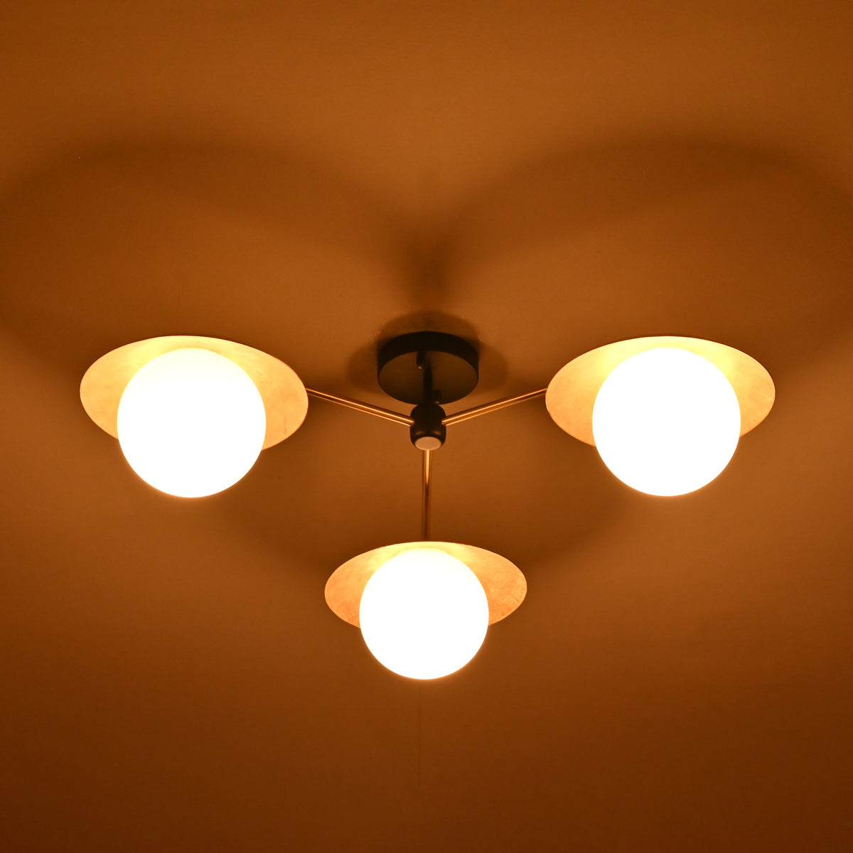 Night view of 3 light brass disc ceiling fixture with opal glass globes creating ambient lighting.