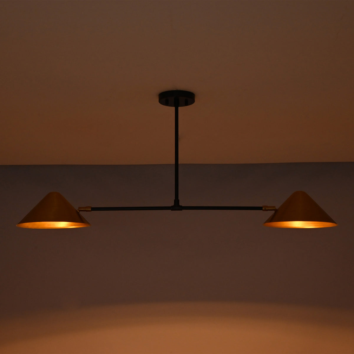 Oslo Modern Double Cone Linear Chandelier with warm illuminated cone shades in low-light setting