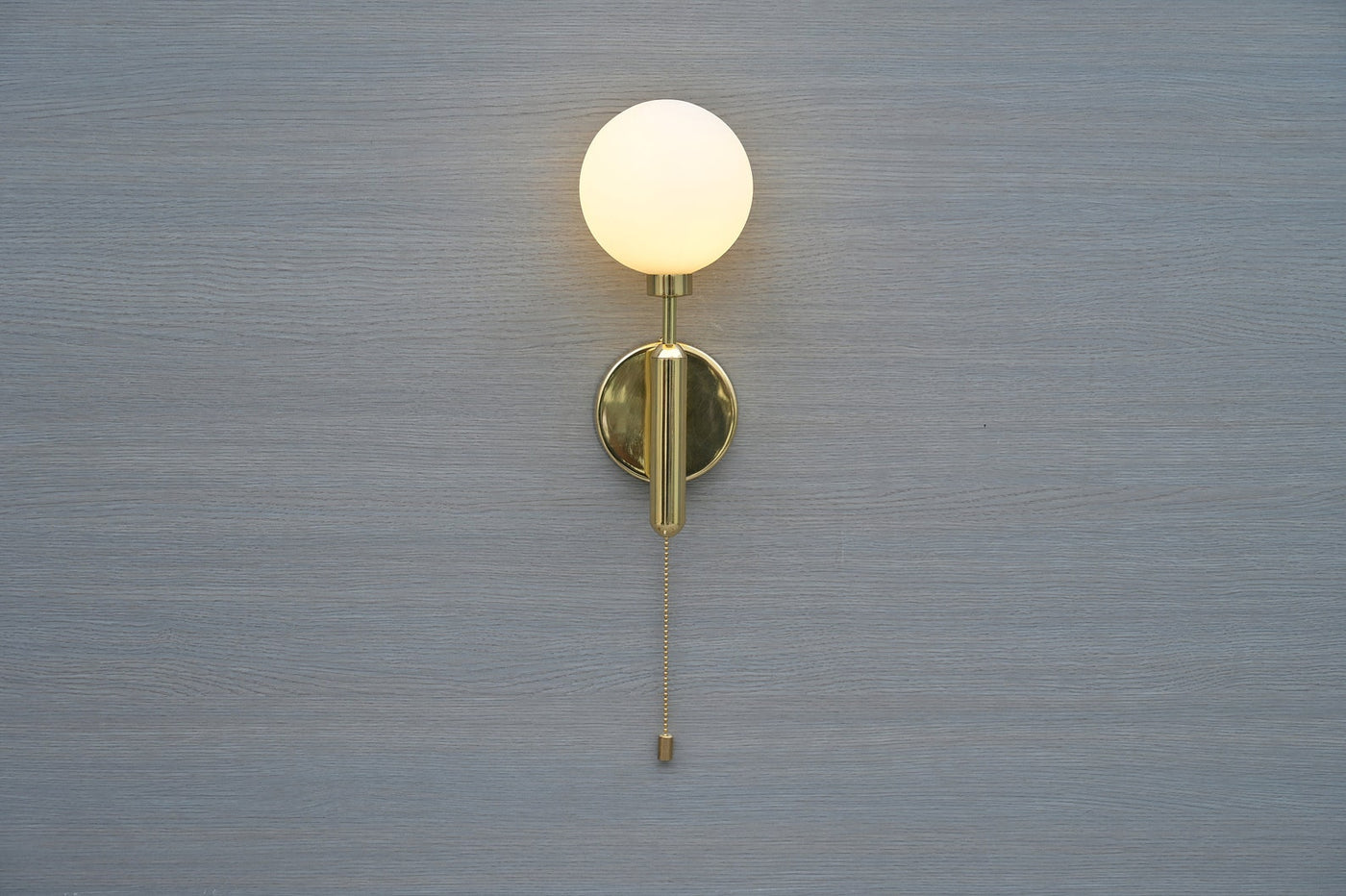 Front view of polished brass wall sconce with opal glass globe and pull chain by Brass Leaf Studio