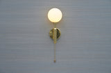 Front view of polished brass wall sconce with opal glass globe and pull chain by Brass Leaf Studio