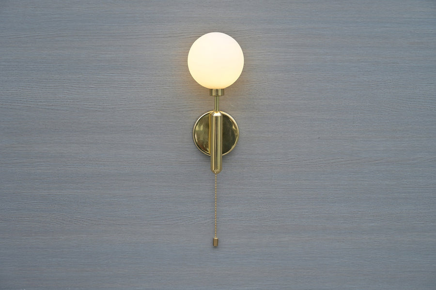 Front view of polished brass wall sconce with opal glass globe and pull chain by Brass Leaf Studio