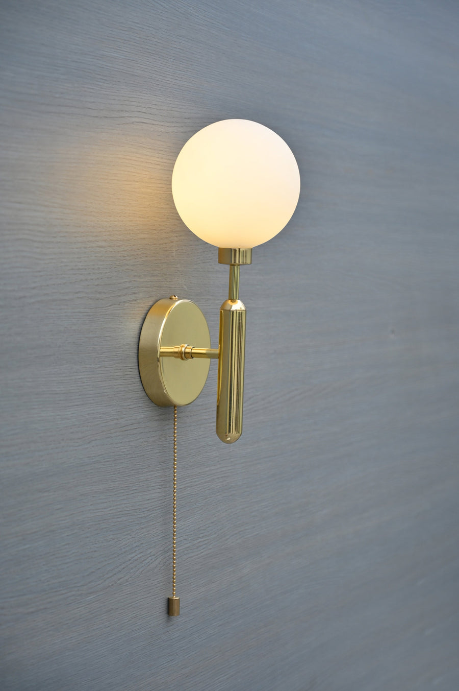 Front view of polished brass wall sconce with opal glass globe and pull chain by Brass Leaf Studio
