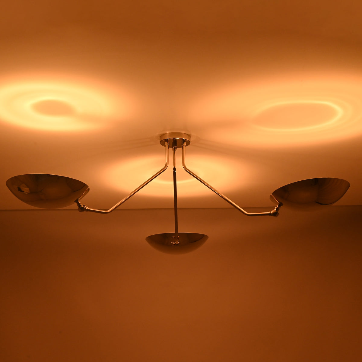 Three light polished chrome ceiling fixture highlighting symmetrical bowl shaped shades and warm glow.