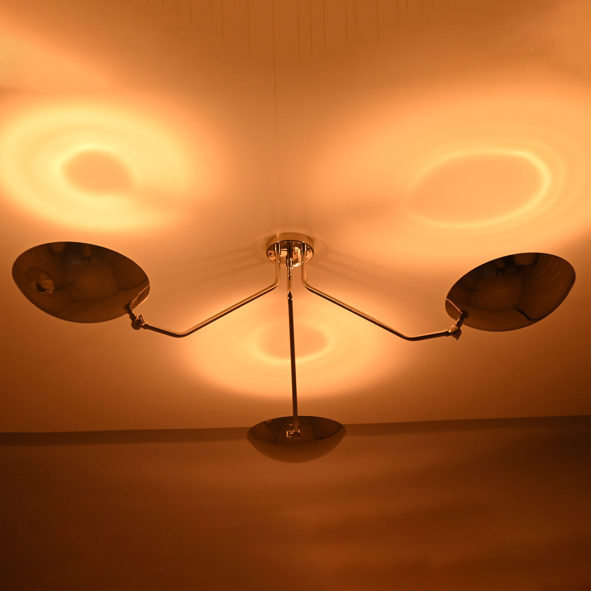 Polished chrome ceiling light casting warm indirect ambient lighting through three brass bowl shades.