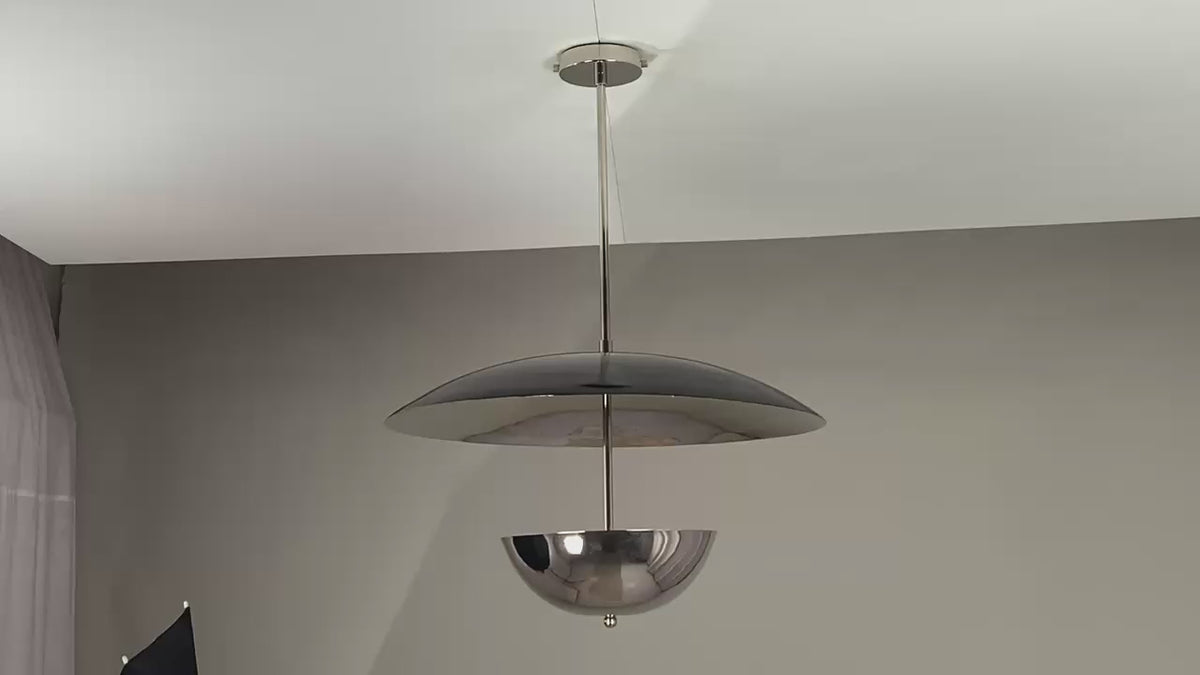 Video showcasing a modern chrome double-dome pendant chandelier rotating slowly under warm ambient lighting, highlighting its reflective finish, sculptural silhouette, and elegant illumination as it casts soft, cinematic glows on surrounding surfaces