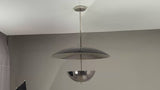 Video showcasing a modern chrome double-dome pendant chandelier rotating slowly under warm ambient lighting, highlighting its reflective finish, sculptural silhouette, and elegant illumination as it casts soft, cinematic glows on surrounding surfaces