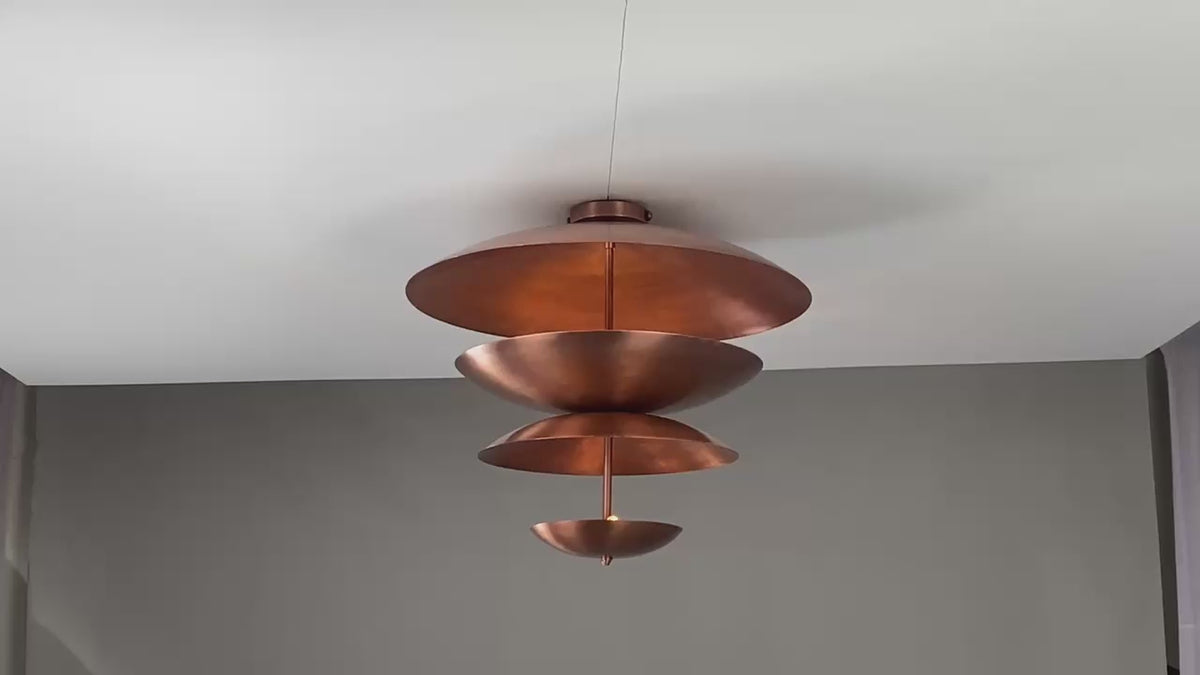 Video of copper disc chandelier showing 360° view, layered design, ambient lighting effect, and sculptural copper finish in daylight and warm glow