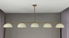 360° view of a modern 72-inch linear brass chandelier with five dome-shaped enamel shades, showcasing warm ambient lighting, minimalist silhouette, and sleek ceiling mount in various room settings.