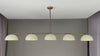 360° view of a modern 72-inch linear brass chandelier with five dome-shaped enamel shades, showcasing warm ambient lighting, minimalist silhouette, and sleek ceiling mount in various room settings.