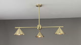Warm-lit modern brass chandelier with three cone-shaped shades, creating cozy ambient lighting in a contemporary living room setting