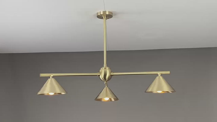 Warm-lit modern brass chandelier with three cone-shaped shades, creating cozy ambient lighting in a contemporary living room setting