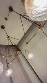 Linear 6-light ribbed glass globe chandelier video showing brass frame, chain suspension, warm glow, and luxury dining room lighting effect