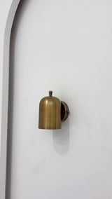 Rome cylindrical brass wall sconce video showing its rounded shade, brass patina finish, compact wall-mounted form and warm focused downward lighting