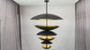 Video showing the Aureon 13-light six tier solid brass disc chandelier with blackened brass outer surfaces, brushed brass interiors, and warm layered glow in luxury interiors