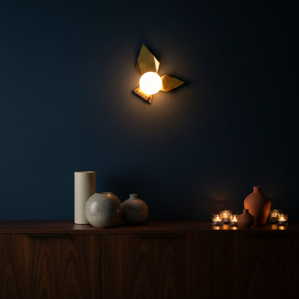 Side view of raw brass artistic wall sconce with layered leaf panels and glowing glass globe shade