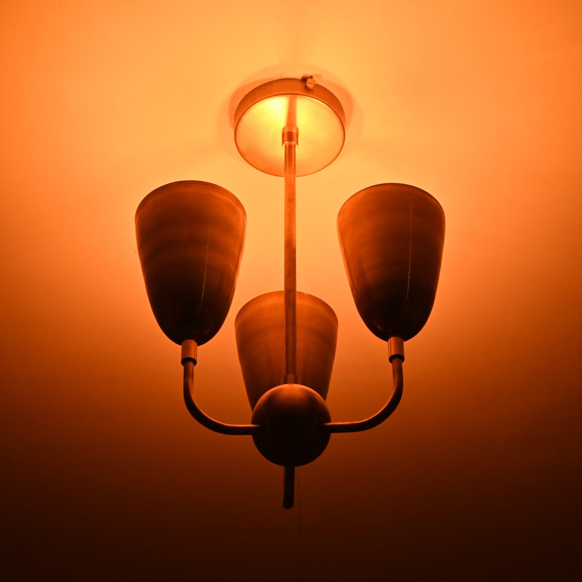 Detailed view of three cone-shaped brass shades connected to brass ceiling base