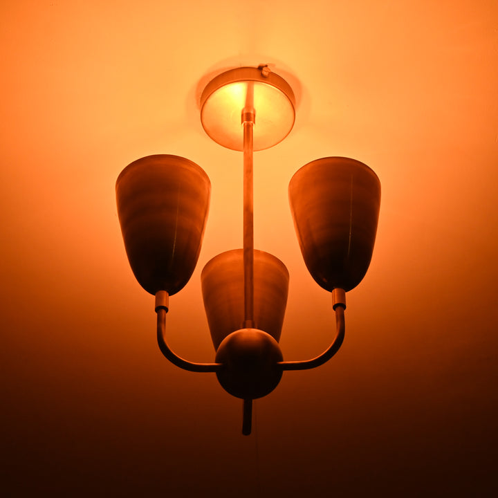 Detailed view of three cone-shaped brass shades connected to brass ceiling base