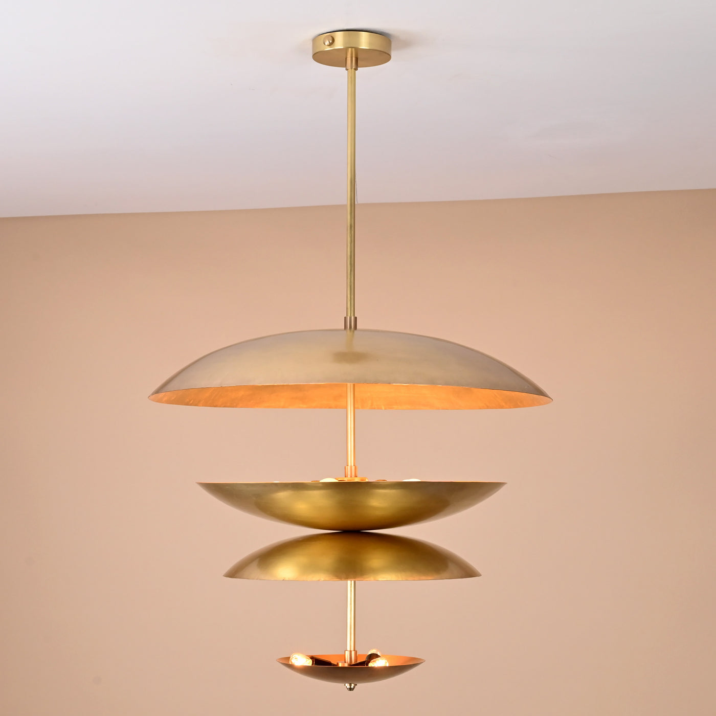 Handcrafted solid brass ceiling light with stacked bowl discs emitting a warm, ambient glow