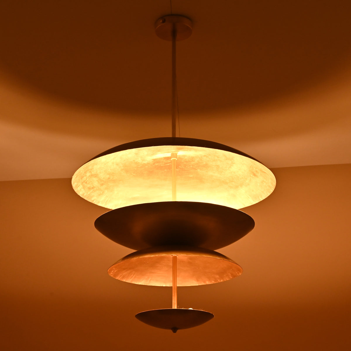 Warm glowing effect of multi-disc brass chandelier highlighting layered sculptural form