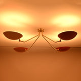 Red disc flush mount chandelier in dark setting creating dramatic indirect lighting with solid brass arms and modern aesthetic.