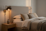 Sculptural ruffled bedside wall sconce with matte black shade, elongated brass stem and warm downward glow