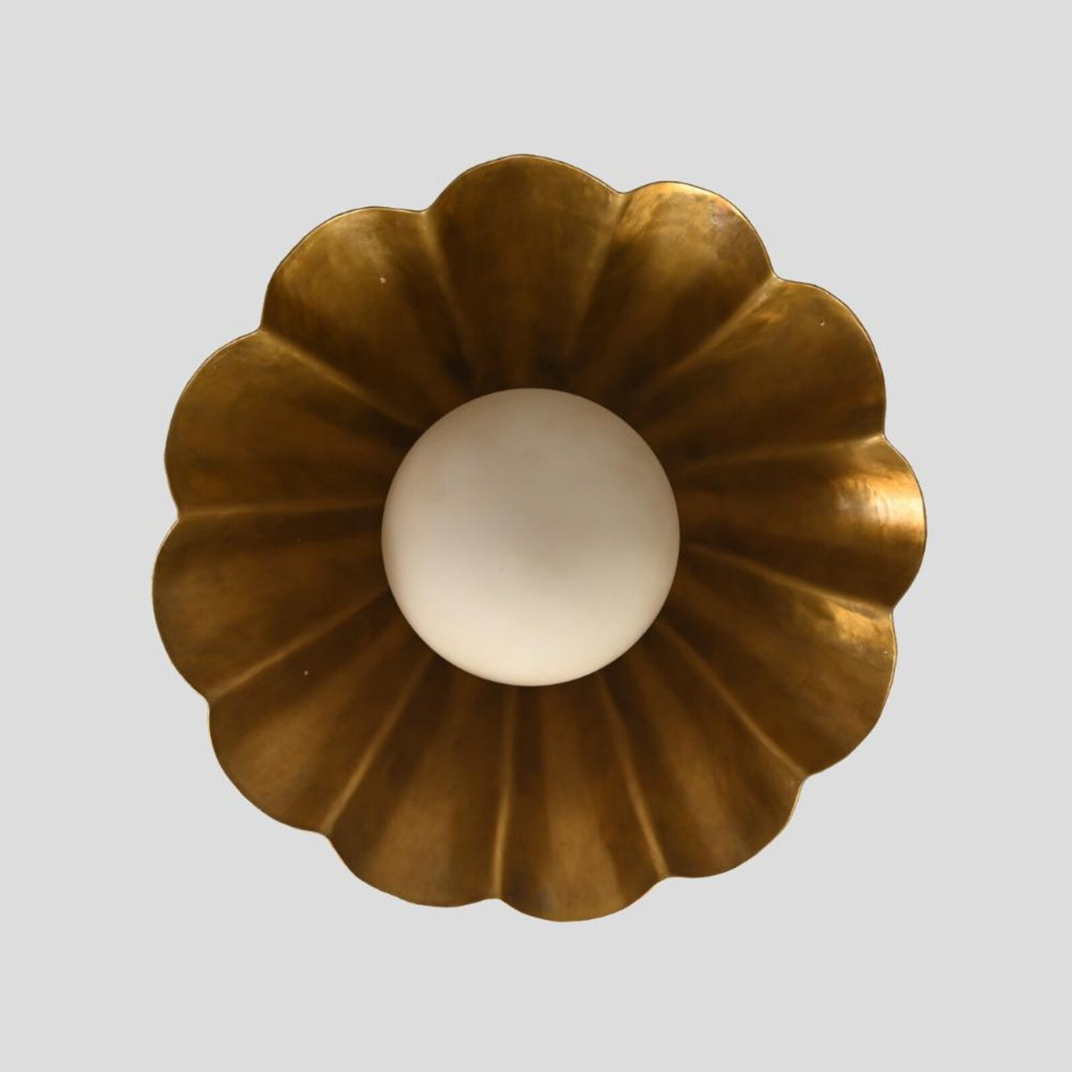 Overhead view of ruffled-edge brass pendant light with circular sculptural shade and globe diffuser, crafted for contemporary and industrial-inspired decor.