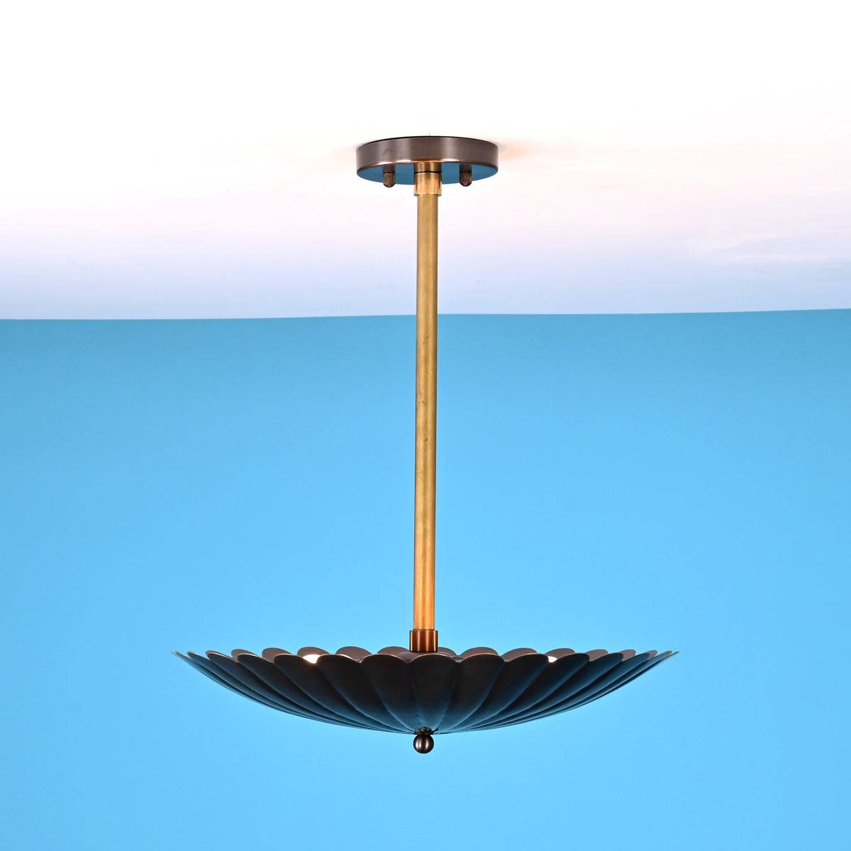 Side view of hanging floral bowl brass pendant light with raw brass rod and upward glow on the ceiling.